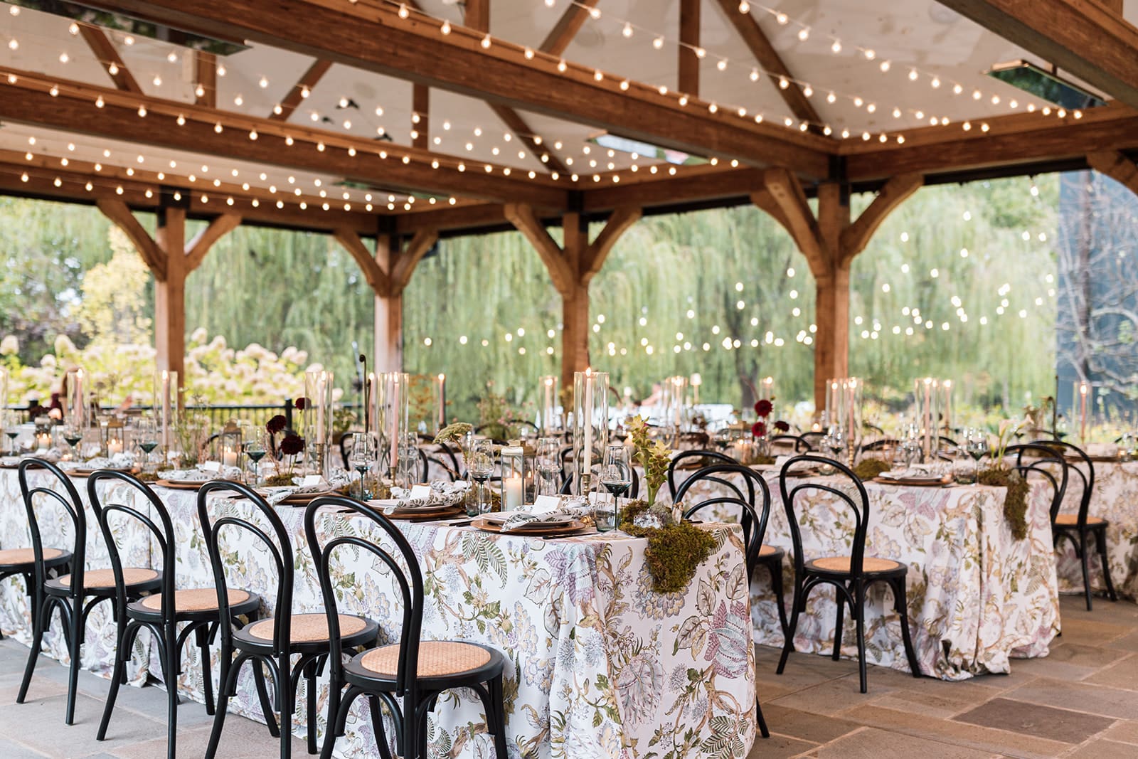 Romantic outdoor pavilion at Clyde’s Willow Creek Farm decorated with patterned linens, candlelight, and bistro lights for an elegant modern-barn dinner.