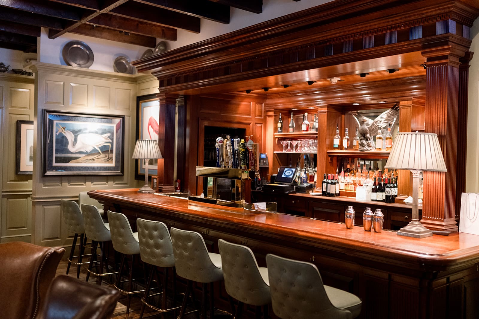 Classic mahogany bar at Clyde’s Willow Creek Farm with tufted barstools, traditional lighting, and vintage artwork.