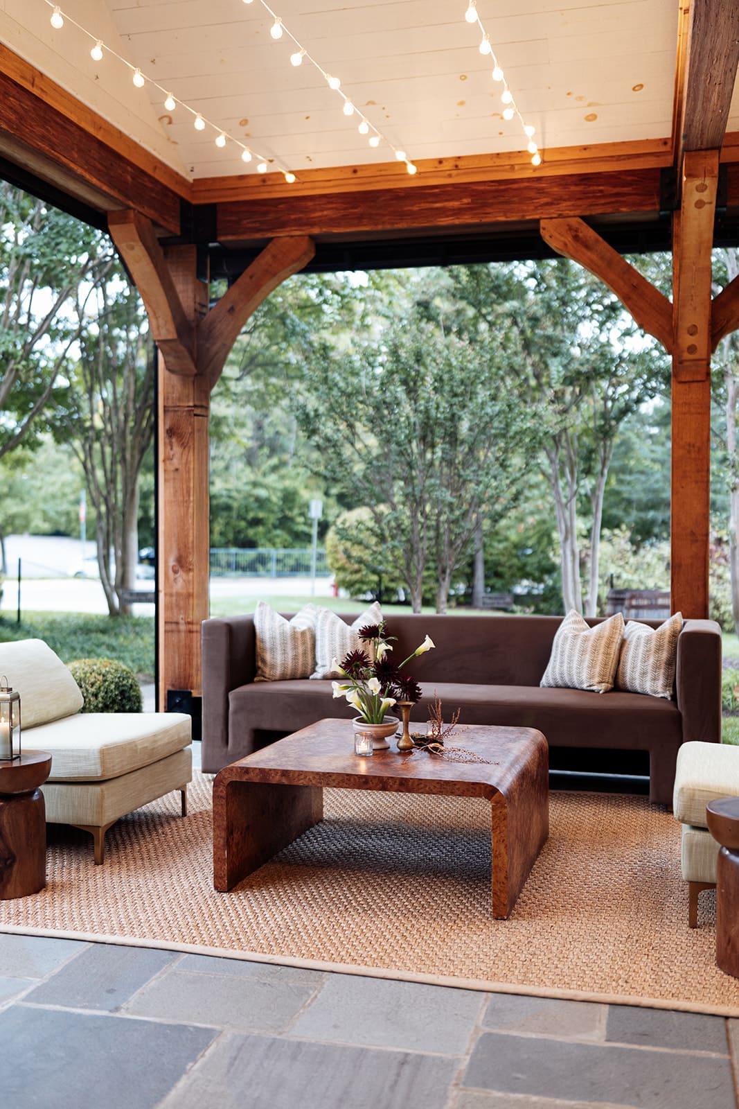 Cozy lounge seating at Clyde’s Willow Creek Farm featuring a brown sofa, wood coffee table, neutral chairs, and soft candlelight under the pavilion.”