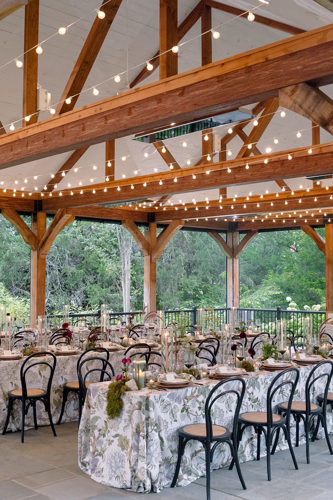 Elegant reception tables beneath bistro lights at Clyde’s Willow Creek Farm, featuring botanical linens, tall candles, and views of the willow trees.