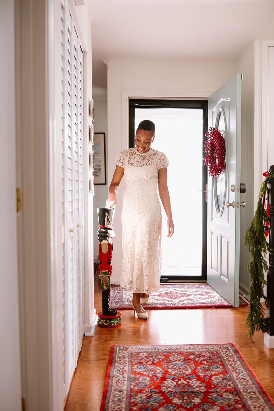 Woman in a lace dress walking through a bright entryway decorated for Christmas.