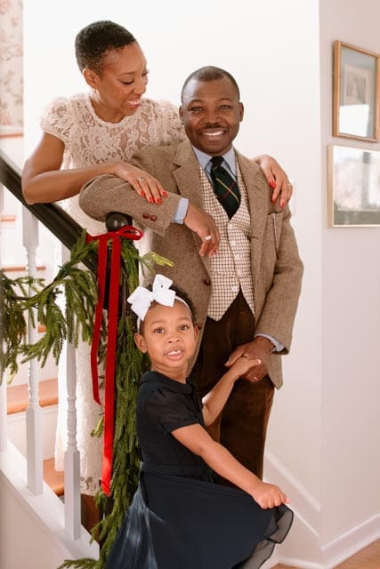 A family poses together on a Christmas-decorated staircase, with greenery and red ribbon along the banister.