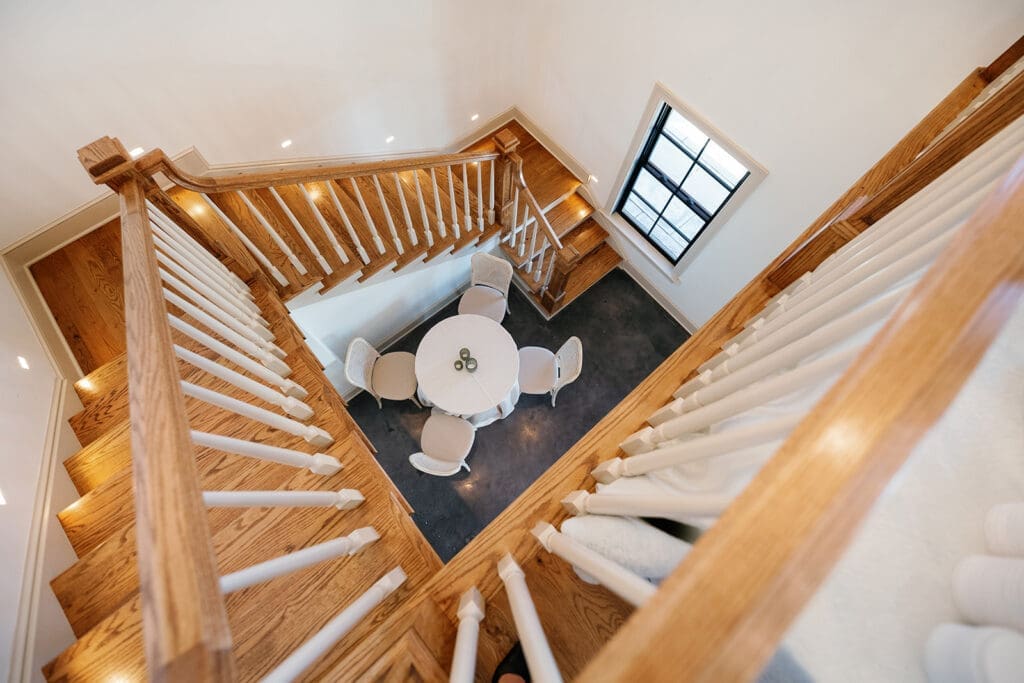 Overhead view of the staircase inside The Manor 1858 with warm wood railings and a round table below.