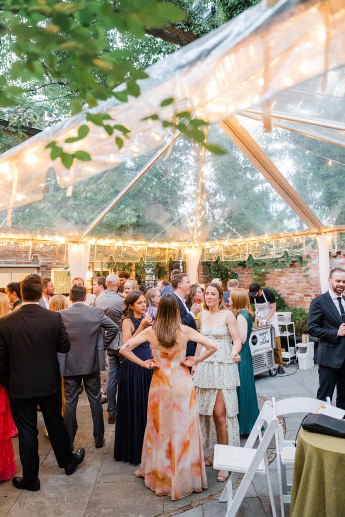 Wedding guests mingling under a clear-top tent at Fathom Gallery Georgetown during cocktail hour, with string lights glowing overhead.