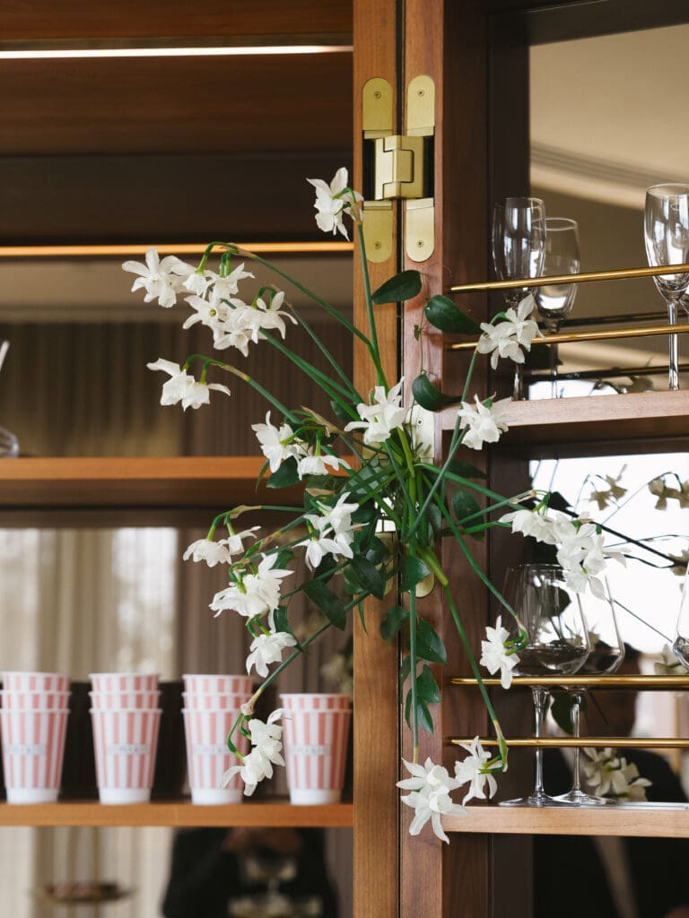 White floral installation styled on a wood and brass bar shelf with glassware and striped cups