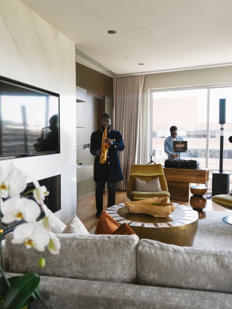 Saxophonist and DJ performing during a wedding-day lounge moment in a modern suite with soft neutral interiors